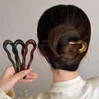 Low twisted bun held by a tortoiseshell-pattern French pin; a hand holds olive, black and burgundy pins