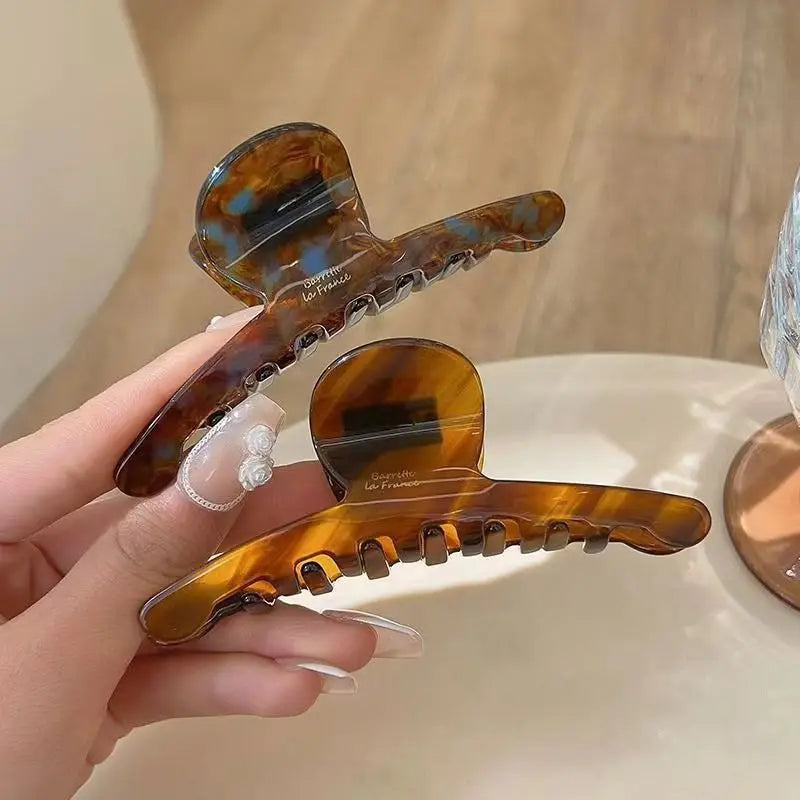 Hand holding two tortoiseshell-pattern claw clips in different shades