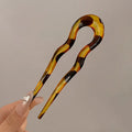 Tortoiseshell-pattern French hair pin in amber and dark brown, held between two fingers