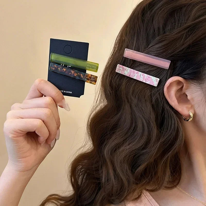Pink marble-look geometric clips worn by the ear; a tortoise and olive set in hand