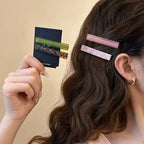 Pink marble-look geometric clips worn by the ear; a tortoise and olive set in hand